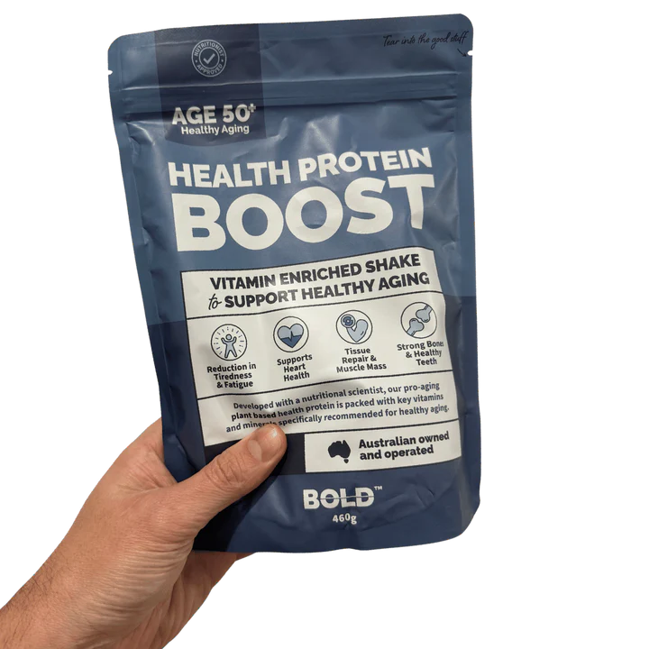 Hand holding a package of 'Health Protein Boost' by AGE 50+ on a white background